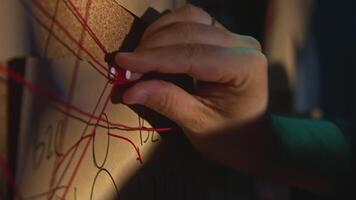 Close-up of board with notes and threads. Stock footage. Man is investigating and fixing evidence on board. Man checks photos and notes on research board video