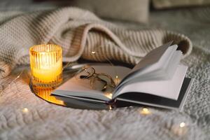 Scented candle with an open book in bed with a warm blanket photo
