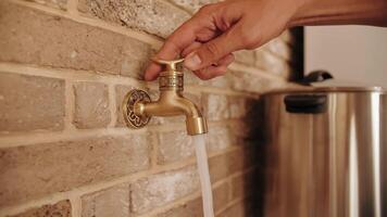The hand turns the handle of the golden faucet in the wall and opens the water. A jet of water runs from a water pipe. video