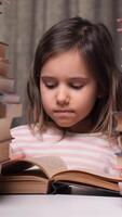 vertical little girl leafing through a book in the library. Stacks of books on the table surround the child. The little girl reads stories from the book with interest. Paper books video
