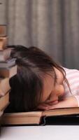 vertical little girl got tired of learning to read and fell asleep on a book. concept of children getting tired of learning. child sleeps on a book surrounded by stacks, symbolizing school stress video