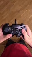 vertical pov First-person view of a gamer holding a black gamepad in his hands, standing on a parquet floor, ready to play videogames. Gamer playing videogames holding a controller video