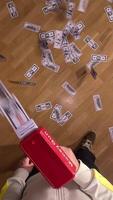 vertical Man having fun shooting fake dollar bills with a toy money gun, causing cash to rain down on a wooden floor. Man shooting fake money with a toy gun. Concept of a big waste of money video