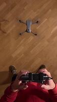 vertical first person view pov Person using a remote control to pilot a drone indoors, hovering above a wooden floor, providing a unique perspective on drone operation video