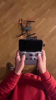vertical pov First-person view Person wearing red sweatshirt piloting compact quadcopter drone using remote controller with smartphone attached indoors over wooden floor video