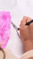 vertical top view little girl Young artist carefully adding details to a colorful cartoon character drawing with a pink marker showcases creativity and imagination in a joyful. close-up video