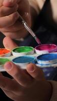 vertical close-up of a child with a brush picking up paint for painting. A set of multi-colored paints for painting with a brush. Children's drawing video