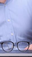 vertical Office worker placing eyeglasses on closed laptop after finishing work on computer, ending workday, taking break from screen time, or protecting laptop screen video