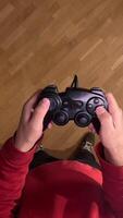 vertical pov first person view Person wearing a red sweatshirt holding a generic wired controller, playing videogames at home. Gamer plays on console. Man quickly presses joystick video