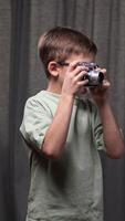 vertical little boy Child photographer focusing through the viewfinder of a vintage rangefinder camera, learning the art of photography against a backdrop of gray curtains video