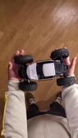 vertical First-person view of a person holding a radio-controlled car indoors on a wooden floor, ready to play and have fun. video
