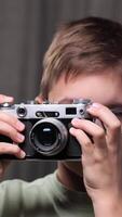 vertical clode-up portrait little Boy learning photography is using an old rangefinder camera, carefully adjusting focus and framing the shot against a gray backdrop. Boy Take a picture video
