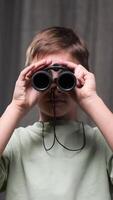 vertical boy looking through binoculars. portrait of boy with binoculars. child peering into distance. concept of close examination. schoolboy looking through binoculars, looking into camera video