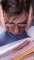 vertical an office worker overloaded with work with documents is tired and clutches his head. The man is upset and clutches his head from the amount of work that has not been done. video