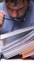 vertical man in glasses overloaded with office work with documents clutches his head from fatigue. upset office worker tired of working with documents. Stressed businessman holding his head video