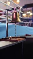 vertical Golden boxing bell hanging on a stand, ready to signal the start or end of a round, with a blurred boxing ring in the background video