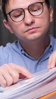 vertical Office worker checking financial documents and searching information in archive folders, sitting at desk and working with paperwork. A man in glasses at a desk in the office video