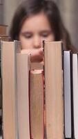 vertical little girl in the library reading a book. education school kid science concept. a child stacks of books flips through the pages reads studies. daughter reading a book lifestyle. video