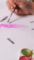 vertical close-up of a child paints draws with a brush and paint on a white sheet of paper. A little girl paints a rabbit with a brush for painting video