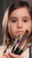 vertical Creative cute girl pose at camera . Young beautiful child looking at camera while standing at room and holding paintbrush. Creative activity. Erudition. child in apron drawing lesson video
