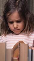 vertical a little girl chooses one book from a multitude of books. a girl leafs through a book. stacks of books surround a little girl. a thoughtful girl searches for something in a book video