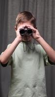 vertical Young boy holds binoculars to his eyes, engaging in imaginative exploration and discovery against a textured backdrop. video