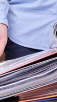 vertical office worker studies a contract, document in the archive, stack of binders. Office worker is searching through a large stack of colorful binders and files, possibly looking for documents video