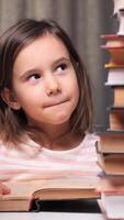 vertical little girl engrossed in her studies, surrounded by a towering stack of books, reading intently and showing curiosity and concentration in a cozy home setting video