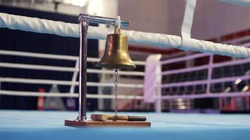 Brass boxing bell hanging from a metal stand with a mallet resting on the wooden base, placed on a blue canvas-covered boxing ring corner video
