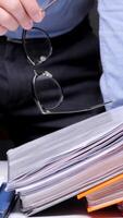 vertical Businessman is holding eyeglasses in his hand over a stack of folders and documents, suggesting a large amount of paperwork and workload video