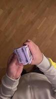 vertical POV first person view Man standing on wooden floor, counting thick stack of hundred dollar bills, evoking wealth, success, and financial stability video
