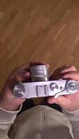 vertical pov First person view Photographer adjusting settings on a vintage rangefinder camera while standing on a wooden parquet floor, seen from a first-person perspective video
