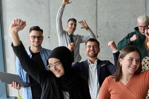 A diverse team of business professionals ecstatically celebrating their success in a modern office, expressing triumph and unity after achieving their goals photo