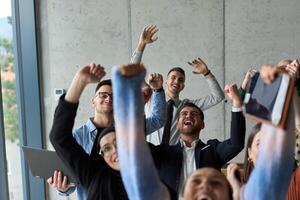 A diverse team of business professionals ecstatically celebrating their success in a modern office, expressing triumph and unity after achieving their goals photo