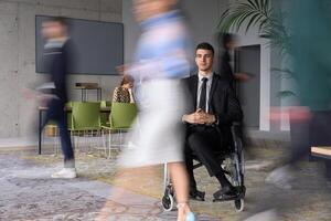 A businessman in a wheelchair navigating through a busy office, surrounded by his colleagues who are actively engaged in their work and collaboration photo