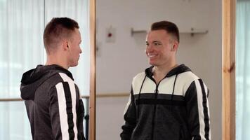 Serious guy stands by mirror and looks at smiling reflection video