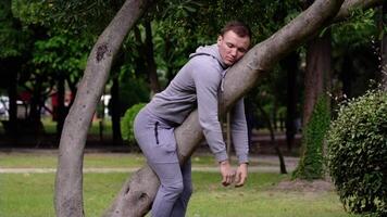 Performer sleeps lying on grey tree trunk as sloth in garden video