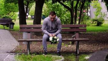 Young man with white flowers sits down on bench in park video