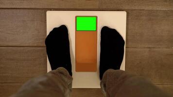 Man in sportswear steps on scales with green screen at home video