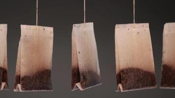 Tea bags on threads hang waved by wind on dark background video