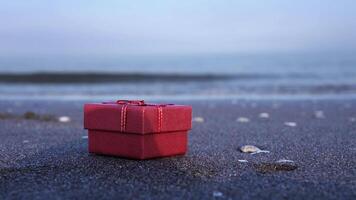 Gift with ribbon and bow on wet sand against running waves video