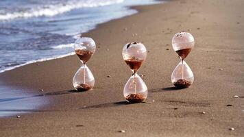Sandglass clocks with golden grains stand on wet sand beach video