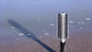 Black and grey hairbrush stands on beach sand washed by sea video