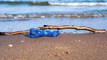 Crumpled bottle and wet stick lie on yellow sandy beach video