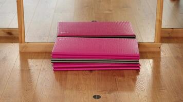 Woman puts coloured roll mats on brown wooden floor in gym video