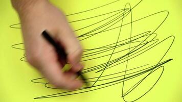 Man draws abstract pattern with black marker on yellow paper video