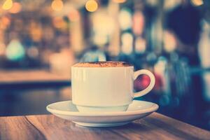 A cup of coffee sits on a table in front of a blurry background photo