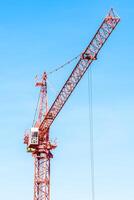 A large red crane is standing in front of a blue sky photo