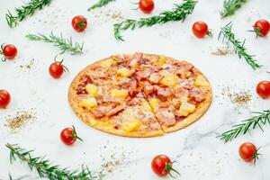 A pizza with ham, pineapple and tomatoes on a marble surface photo