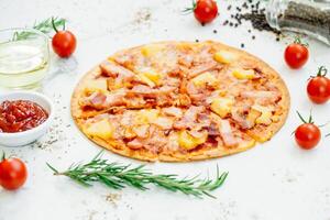 A pizza with ham, tomatoes and herbs on a white table photo